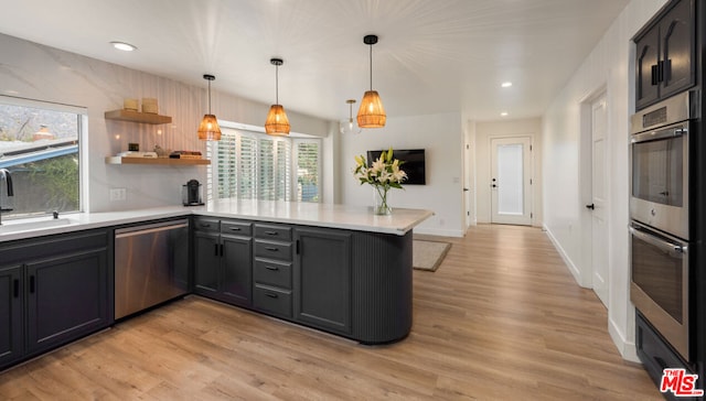 kitchen featuring appliances with stainless steel finishes, sink, hanging light fixtures, kitchen peninsula, and light wood-type flooring