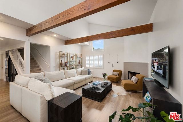 living room with vaulted ceiling with beams, a tile fireplace, and light hardwood / wood-style flooring