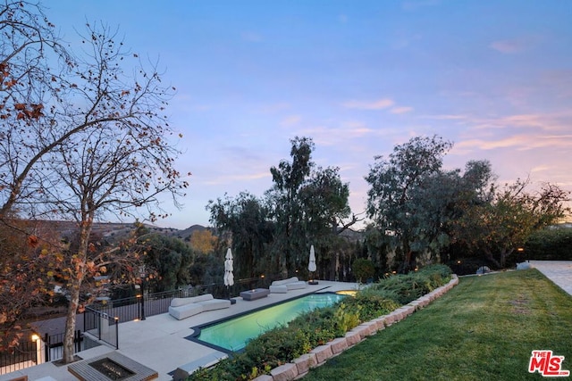 pool at dusk featuring a lawn, a mountain view, and a patio