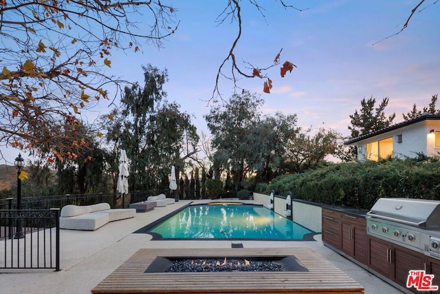 pool at dusk with a patio, a grill, and a fire pit