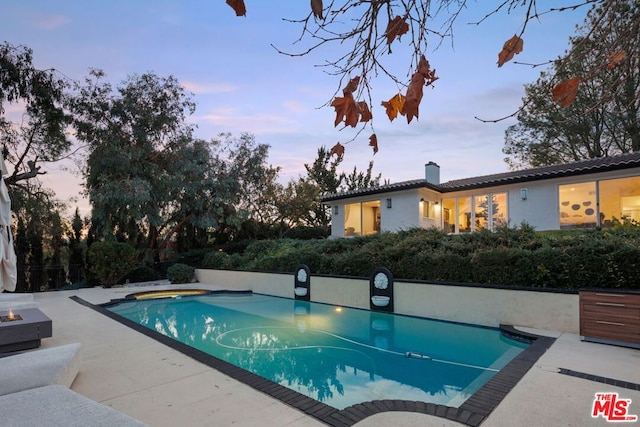 pool at dusk featuring a fire pit and a patio