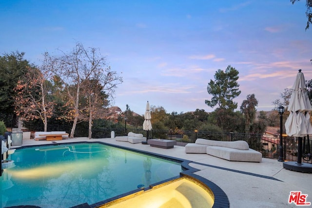 pool at dusk with an in ground hot tub and a patio