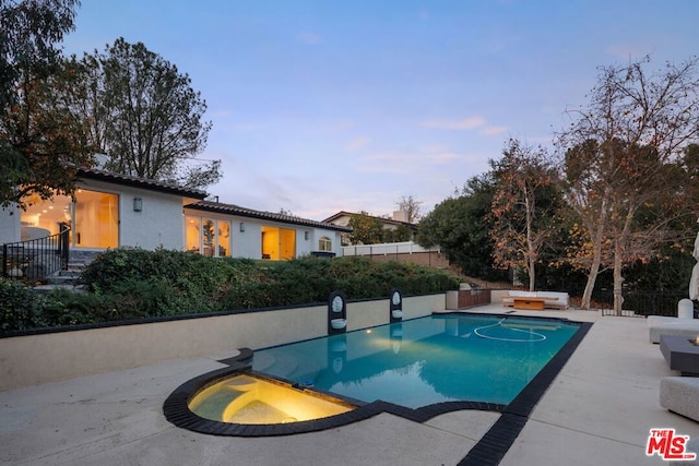 pool at dusk featuring an in ground hot tub and a patio