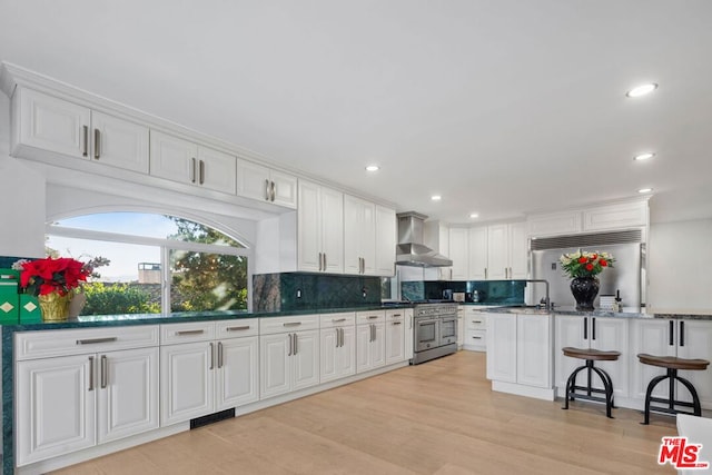 kitchen with white cabinetry, wall chimney exhaust hood, high quality appliances, and dark stone counters