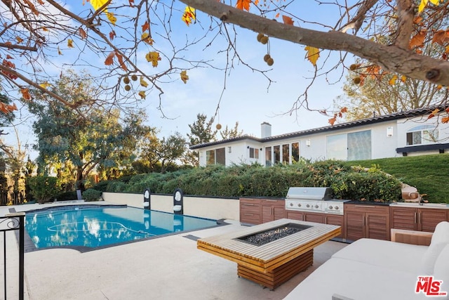 view of pool with a patio area, a fire pit, an outdoor kitchen, and area for grilling