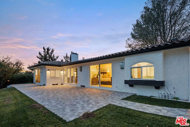 back house at dusk featuring a yard and a patio