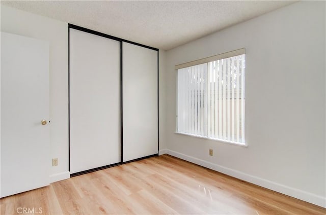 unfurnished bedroom featuring a textured ceiling, a closet, light hardwood / wood-style flooring, and multiple windows