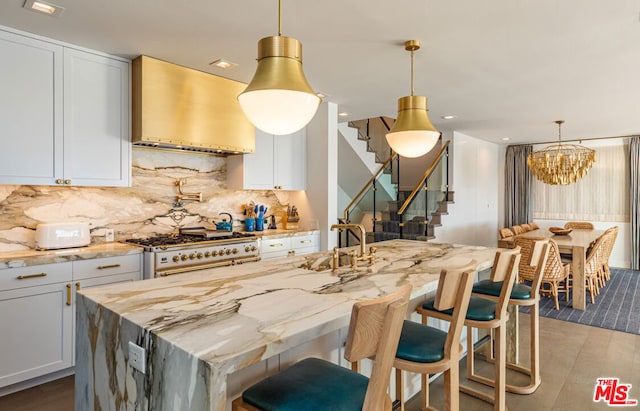 kitchen featuring an island with sink, high end stove, extractor fan, and white cabinetry