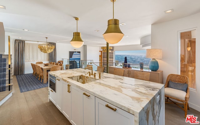 kitchen with white cabinetry, decorative light fixtures, a kitchen island, light stone counters, and sink