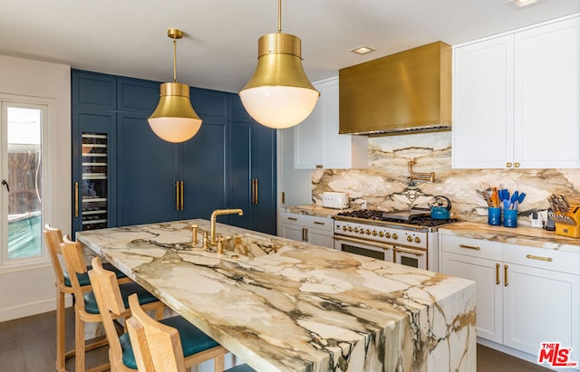 kitchen featuring wall chimney range hood, white cabinetry, decorative backsplash, double oven range, and light stone counters