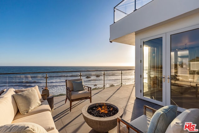 balcony with a water view, an outdoor living space with a fire pit, and a view of the beach