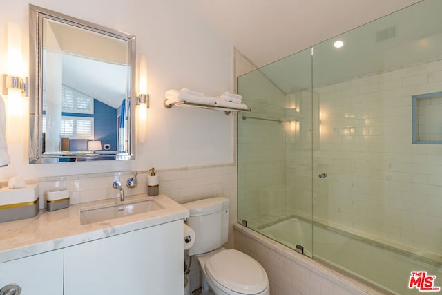 full bathroom with toilet, vanity, vaulted ceiling, tile walls, and enclosed tub / shower combo