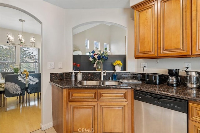 kitchen with stainless steel dishwasher, sink, hanging light fixtures, dark stone counters, and a chandelier