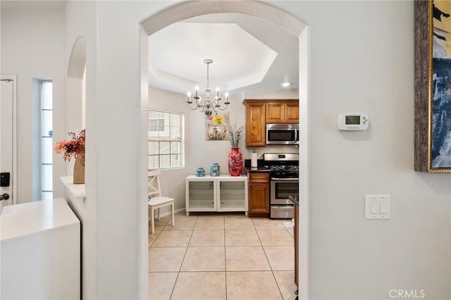 kitchen with pendant lighting, appliances with stainless steel finishes, a raised ceiling, a notable chandelier, and light tile patterned floors