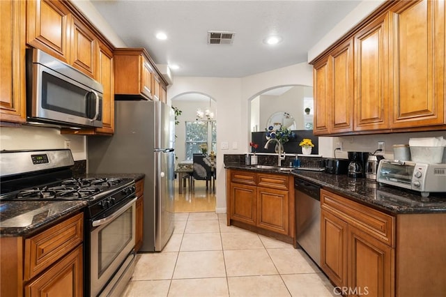 kitchen with light tile patterned floors, stainless steel appliances, a notable chandelier, and dark stone countertops