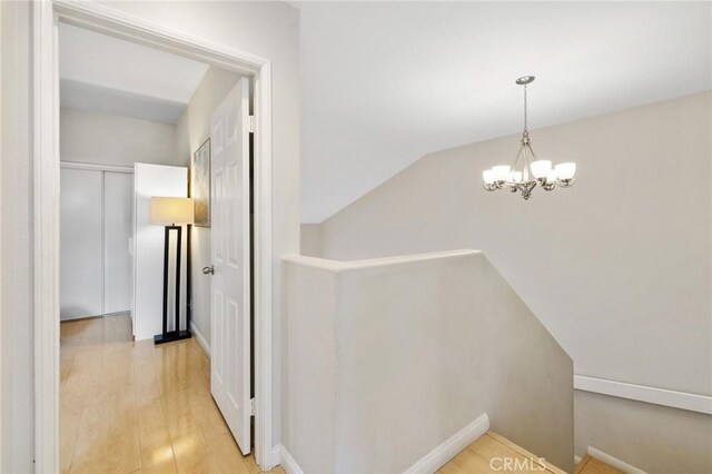 corridor featuring lofted ceiling, light wood-type flooring, and an inviting chandelier