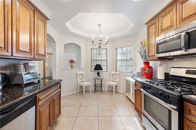 kitchen with an inviting chandelier, light tile patterned flooring, a tray ceiling, and stainless steel appliances