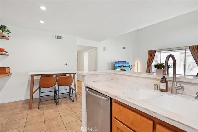 kitchen with a breakfast bar area, light tile patterned flooring, light stone countertops, stainless steel dishwasher, and sink