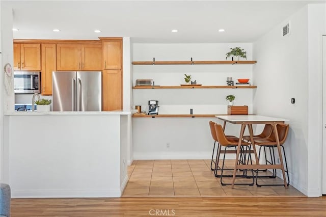 kitchen with light wood-type flooring, appliances with stainless steel finishes, a kitchen bar, and kitchen peninsula