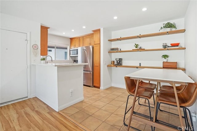 kitchen featuring stainless steel appliances, sink, a kitchen breakfast bar, kitchen peninsula, and light wood-type flooring