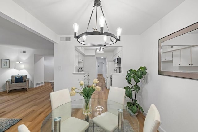 dining area featuring sink, light hardwood / wood-style flooring, and an inviting chandelier