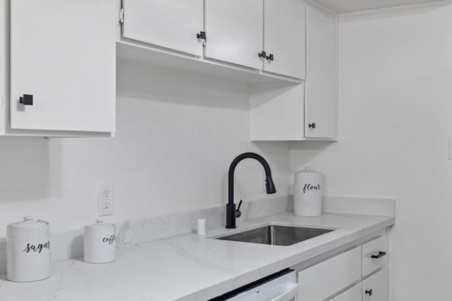 kitchen featuring light stone counters, sink, and white cabinets