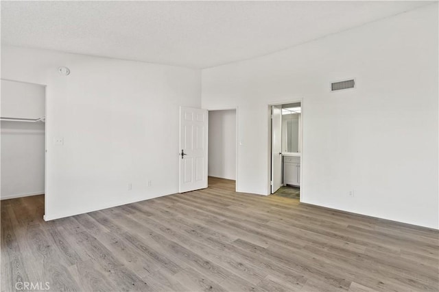 unfurnished bedroom featuring ensuite bathroom, a walk in closet, a closet, and light hardwood / wood-style flooring