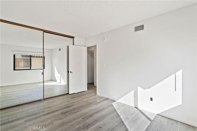 unfurnished bedroom with light hardwood / wood-style floors, a textured ceiling, and a closet