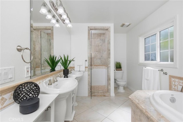 bathroom with tiled bath, toilet, dual sinks, and tile patterned flooring