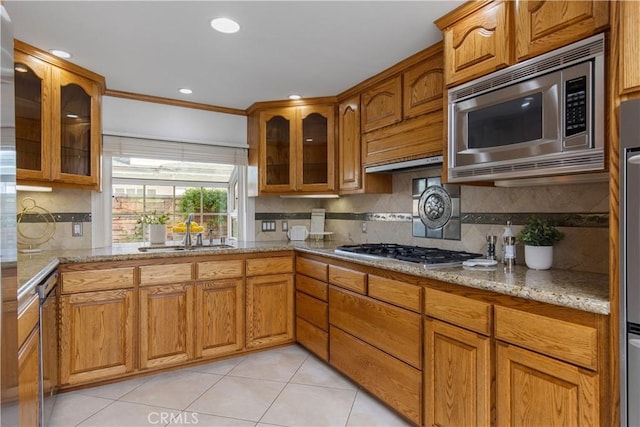 kitchen with appliances with stainless steel finishes, backsplash, light tile patterned flooring, light stone countertops, and sink