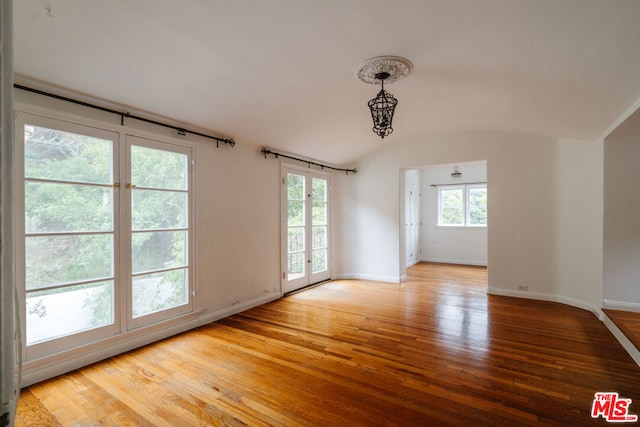 empty room with hardwood / wood-style floors, lofted ceiling, and a notable chandelier