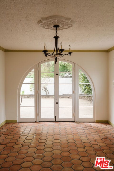 interior space with a textured ceiling, ornamental molding, french doors, and a notable chandelier