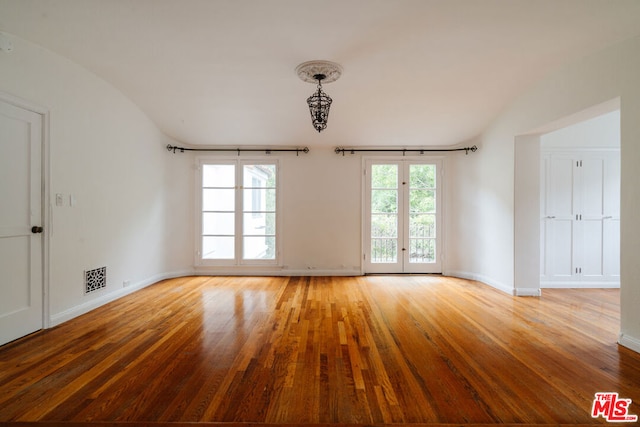 empty room featuring light wood-type flooring, vaulted ceiling, and french doors