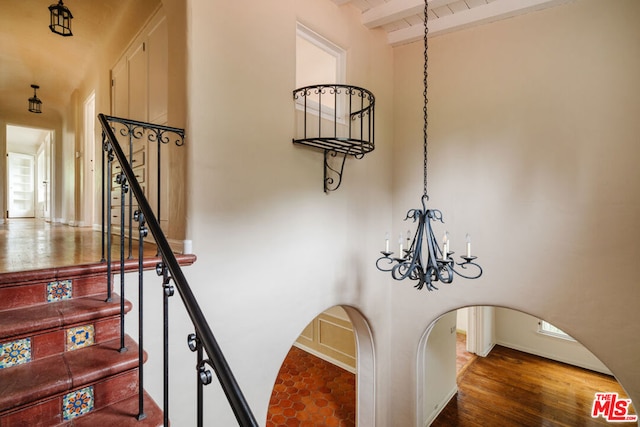 stairs featuring beam ceiling, an inviting chandelier, and hardwood / wood-style flooring