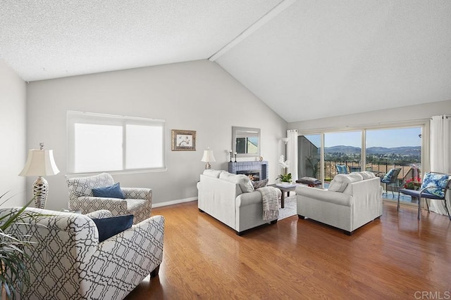 living room with hardwood / wood-style flooring, a textured ceiling, a tiled fireplace, a mountain view, and vaulted ceiling