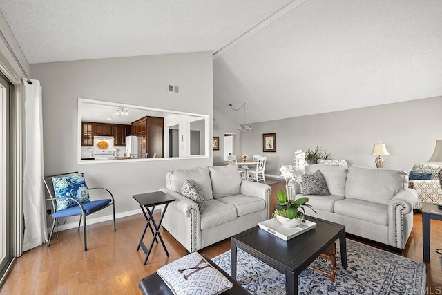 living room with lofted ceiling, a chandelier, and light hardwood / wood-style floors