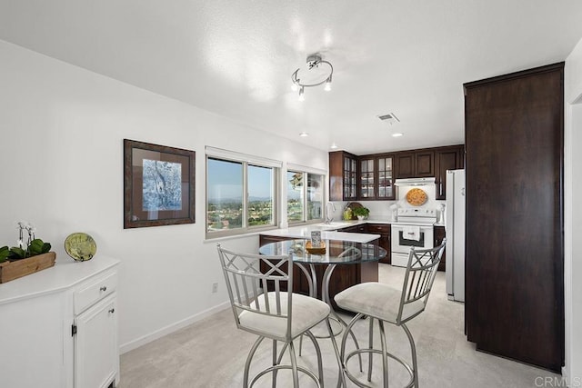 kitchen with white appliances, dark brown cabinets, a kitchen breakfast bar, a kitchen island, and light colored carpet