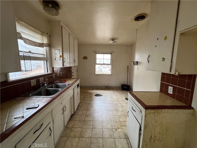 kitchen with tasteful backsplash, white cabinets, sink, and tile countertops