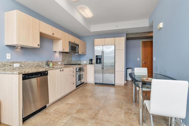 kitchen with decorative backsplash, sink, appliances with stainless steel finishes, light brown cabinetry, and light stone counters