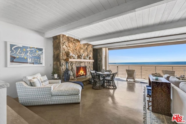 living room featuring concrete flooring, a water view, a stone fireplace, and beamed ceiling