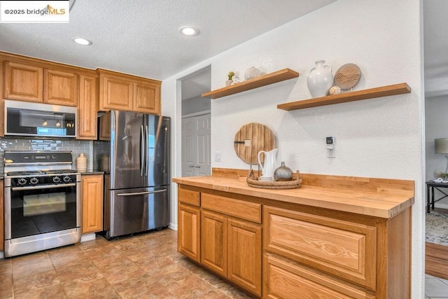 kitchen with a textured ceiling, stainless steel appliances, backsplash, and wooden counters