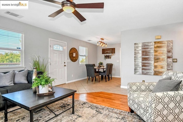 tiled living room featuring ceiling fan with notable chandelier