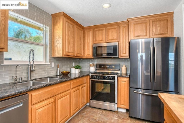 kitchen with decorative backsplash, sink, dark stone countertops, and stainless steel appliances