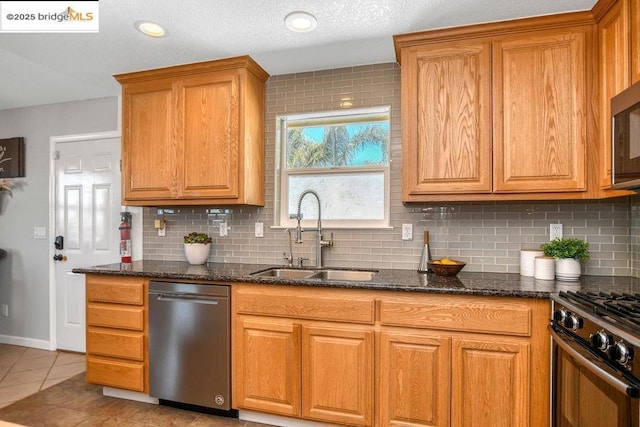 kitchen with light tile patterned floors, stainless steel appliances, dark stone countertops, and sink