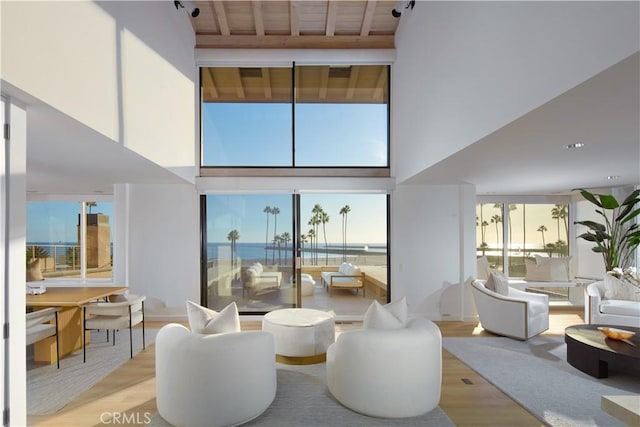 living room with a towering ceiling, wooden ceiling, light hardwood / wood-style flooring, and a water view