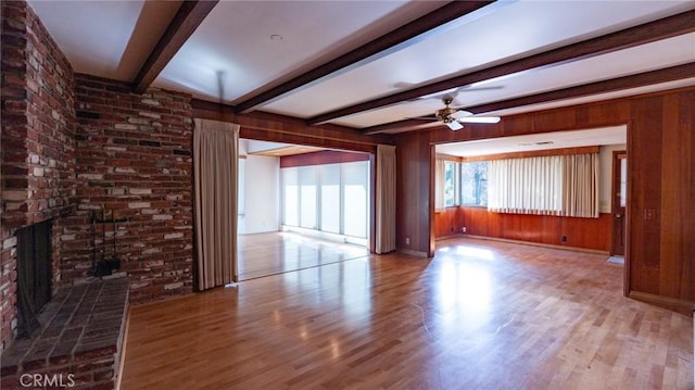 unfurnished living room with ceiling fan, hardwood / wood-style flooring, wood walls, a brick fireplace, and beam ceiling