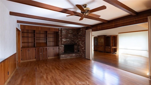 unfurnished living room with ceiling fan, a fireplace, hardwood / wood-style flooring, and wooden walls