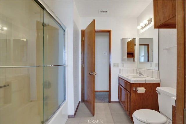 full bathroom featuring toilet, bath / shower combo with glass door, tile patterned flooring, and vanity