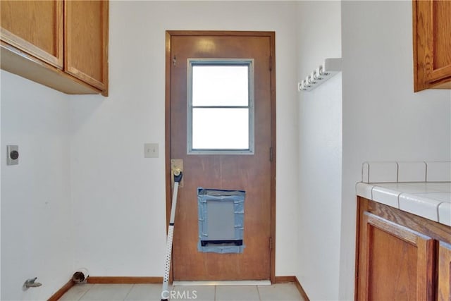 laundry area with electric dryer hookup, cabinets, and light tile patterned floors