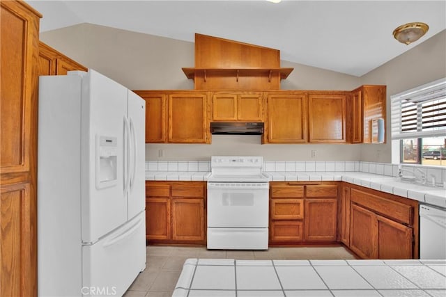 kitchen with white appliances, vaulted ceiling, tile countertops, light tile patterned floors, and sink